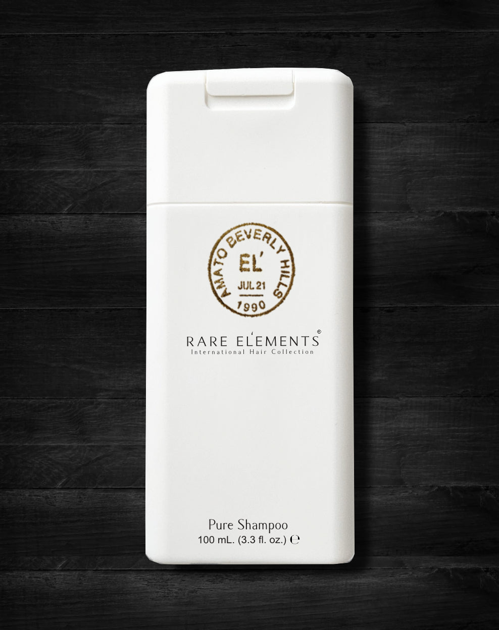 A travel-size shampoo bottle with a white label, branded as 'Rare Elements' on a dark wooden surface.